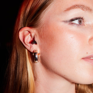 Close-up of an ear wearing a discreet black Happy Ears earplug with gold jewellery